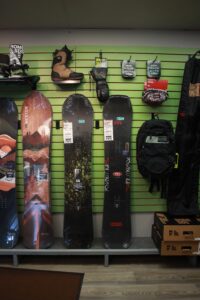 Rome, Weston, and venture snowboards, accessories, and boots up against green wall at Bicycle Experience